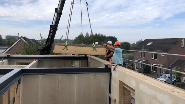 Crane installation of a Dun Agro prefabricated timber-framed hempcrete wall panel, serving as a monolithic, carbon-negative building envelope.