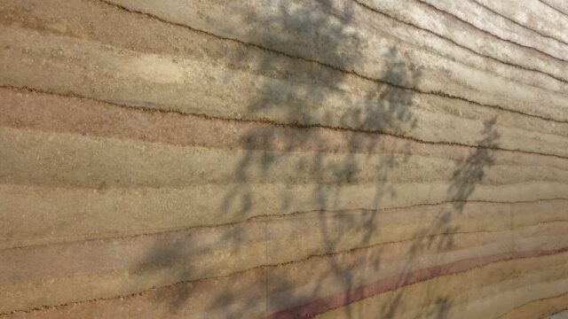 Load-bearing structural insulated rammed earth wall by SIREWALL, demonstrating geological stratification and high compressive strength.